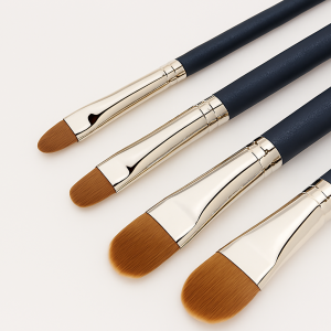 Four premium makeup brushes in graduated sizes displayed diagonally on a clean white background, featuring navy blue handles, silver ferrules, and soft brown synthetic bristles.