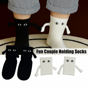 A person wearing mismatched black and white socks with cartoon eyes and fabric arms holding hands, standing on a cream and black striped rug. Additional pairs of the socks are displayed below with the label 'Fun Couple Holding Socks.