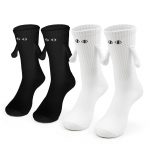 Four whimsical socks—two black and two white—each featuring embroidered eyes and tiny arms, arranged side by side on a neutral background.