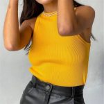 A person wearing a sleeveless yellow ribbed top and black leather pants. The person has long dark hair and is accessorized with a pearl necklace.