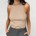 A woman wearing a beige ribbed sleeveless tank top paired with gray trousers and a gold chain necklace.