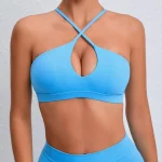 Model wearing a cobalt blue halter bra and matching leggings with crisscross neckline and teardrop cutout, standing against a light wall