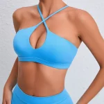 Model wearing a cobalt blue halter bra and matching leggings with crisscross neckline and teardrop cutout, standing against a light wall