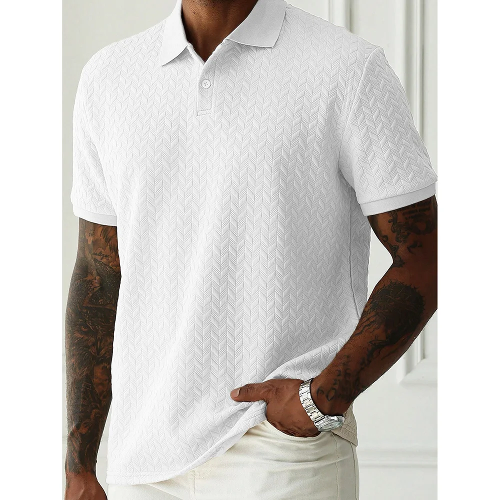Model wearing a white herringbone-textured polo shirt with short sleeves, tattoos on both arms, and a silver wristwatch, standing indoors against a white wall.
