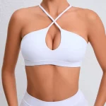 Model wearing a pure white halter bra with crisscross straps and teardrop keyhole cutout, standing against a light wall