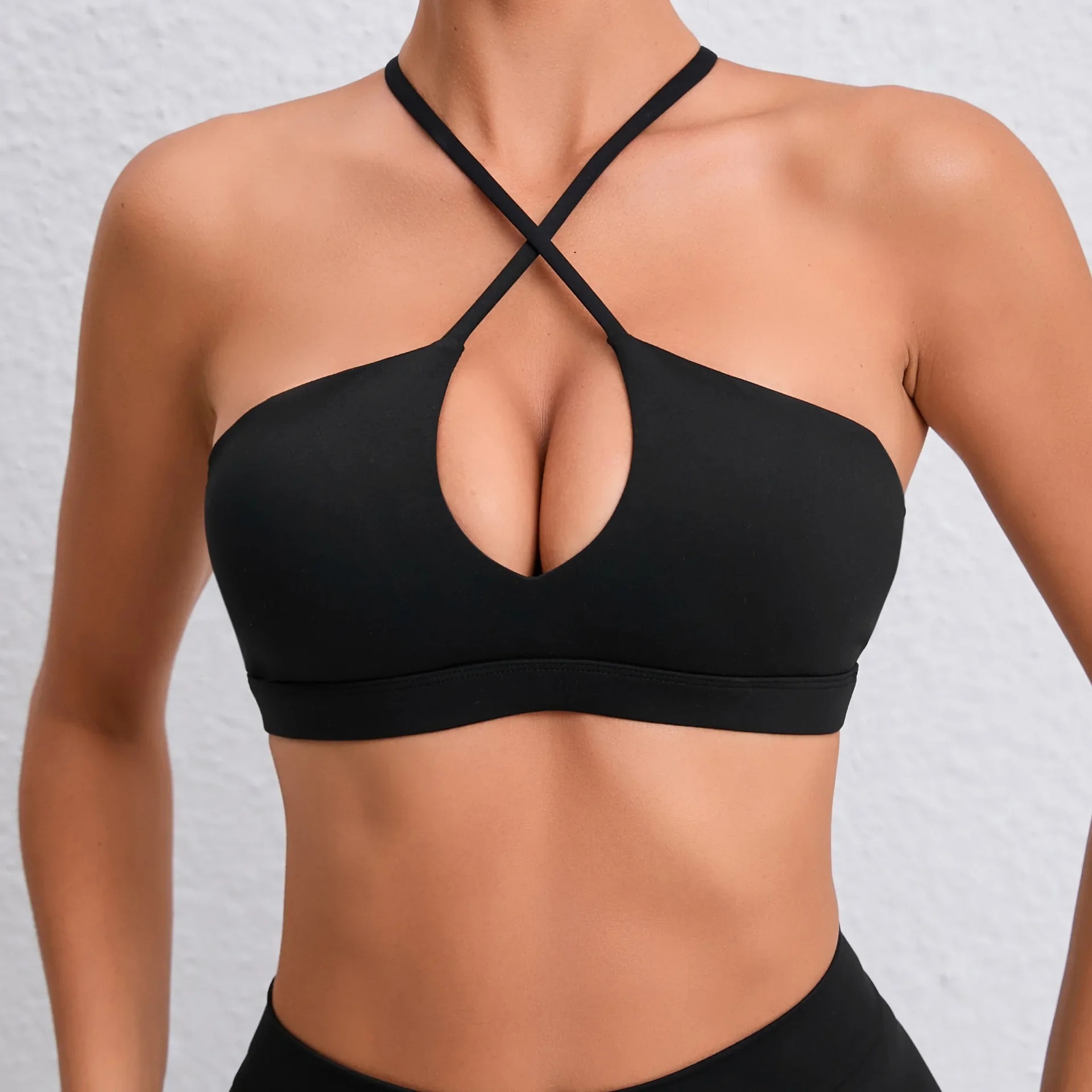 Model wearing a jet black halter bra with crisscross neckline and central keyhole cutout against a light wall