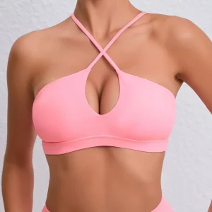 Model wearing a soft rose halter-style bra with crisscross neckline and teardrop cutout against a white textured wall