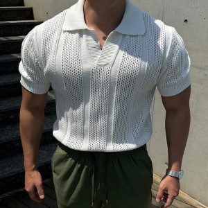 Man wearing a white short-sleeved textured knit polo shirt and olive green drawstring pants, standing outdoors near concrete steps and wall