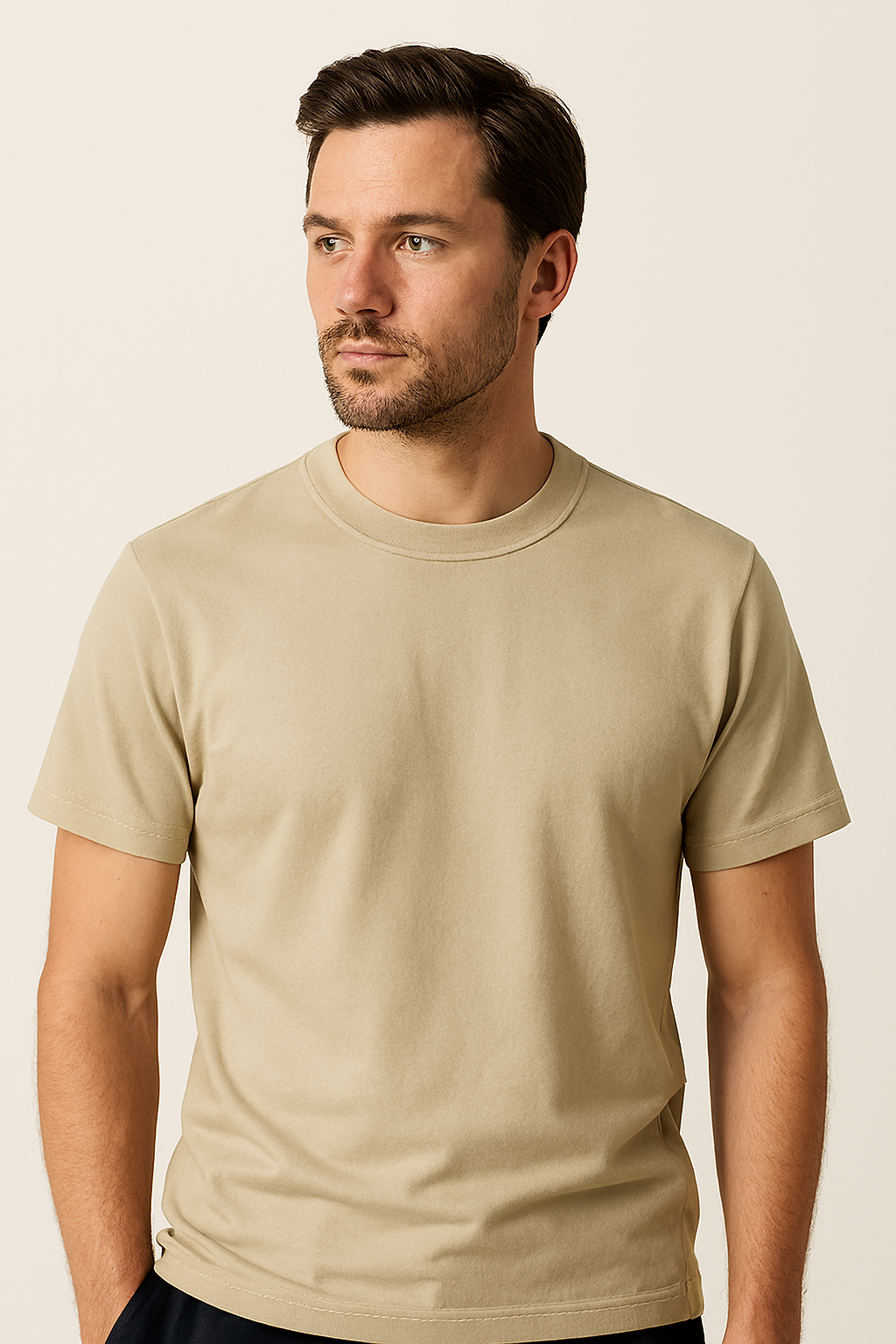 Young man wearing a beige crewneck T-shirt, standing against a neutral background with a calm expression.