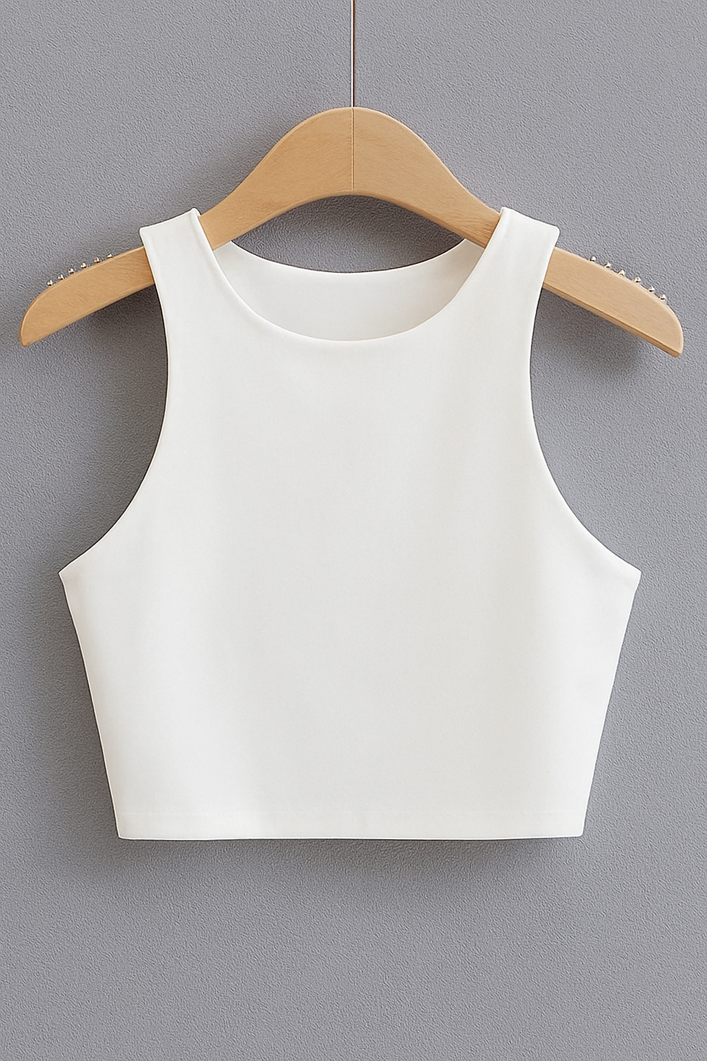 White sleeveless crop top on wooden hanger against gray fabric backdrop.